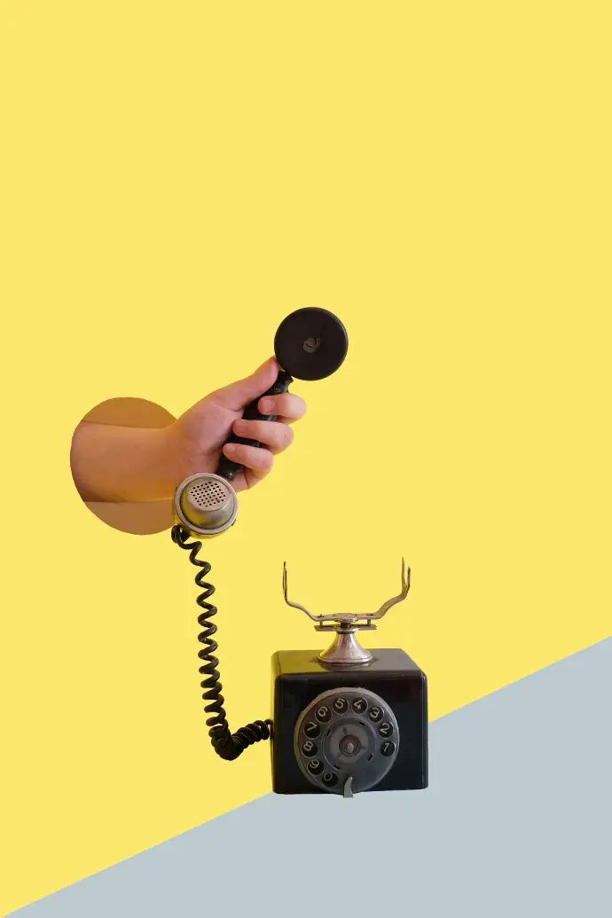 Person hält den Hörer eines schwarzen Wählscheibentelefons.