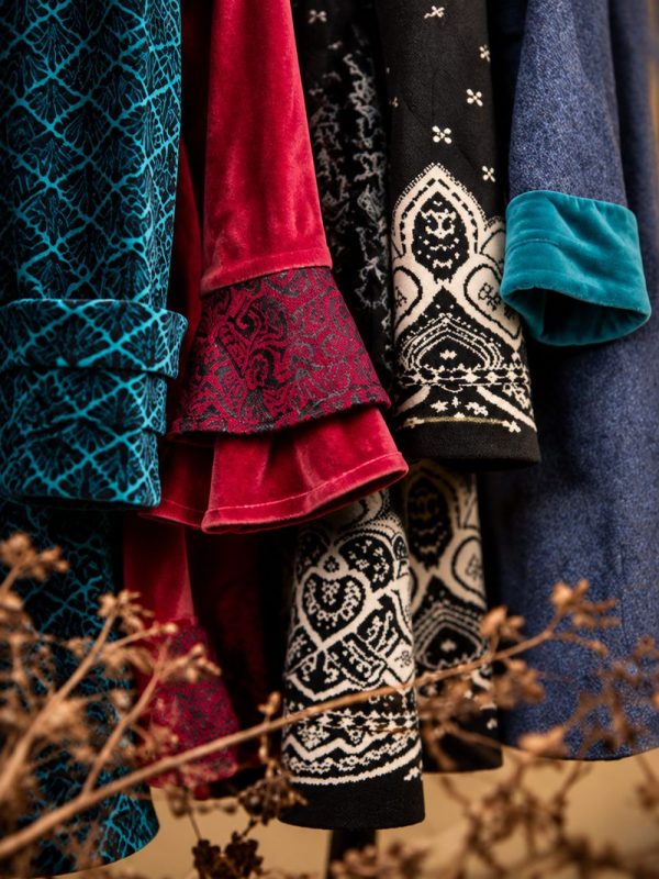 Ärmel mehrerer Mäntel nebeneinander: Samt in Petrol und Rot, Brokat, Strick-Jacquard in Schwarz und Creme