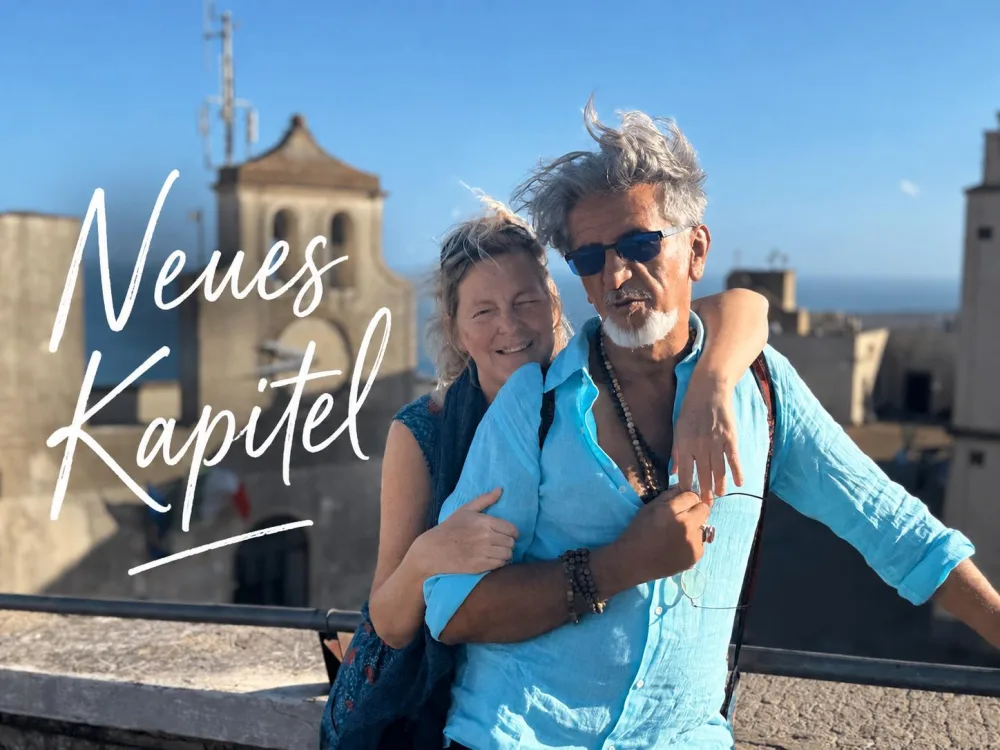Gisela und Hamid Arm in Arm auf einer Terrasse über dem Meer, daneben der Schriftzug „Neues Kapitel“