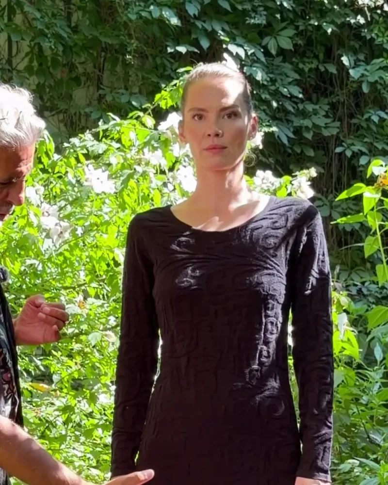 Hamid zeigt auf das gerade geschnittene Strickkleid Nusha, das Elisabeth über einer weiten schwarzen Hose trägt