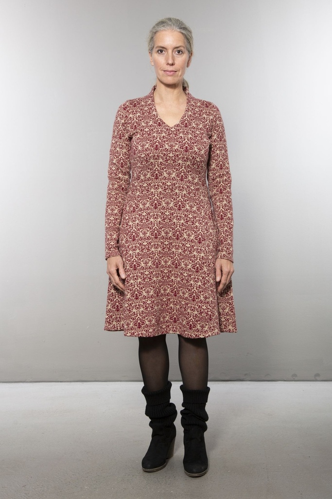 Ganzkörperansicht von vorn: knielanges Strickkleid mit rot-weißem Ornamentmuster, V-Ausschnitt, langärmelig, der Rock fällt leicht ausgestellt.