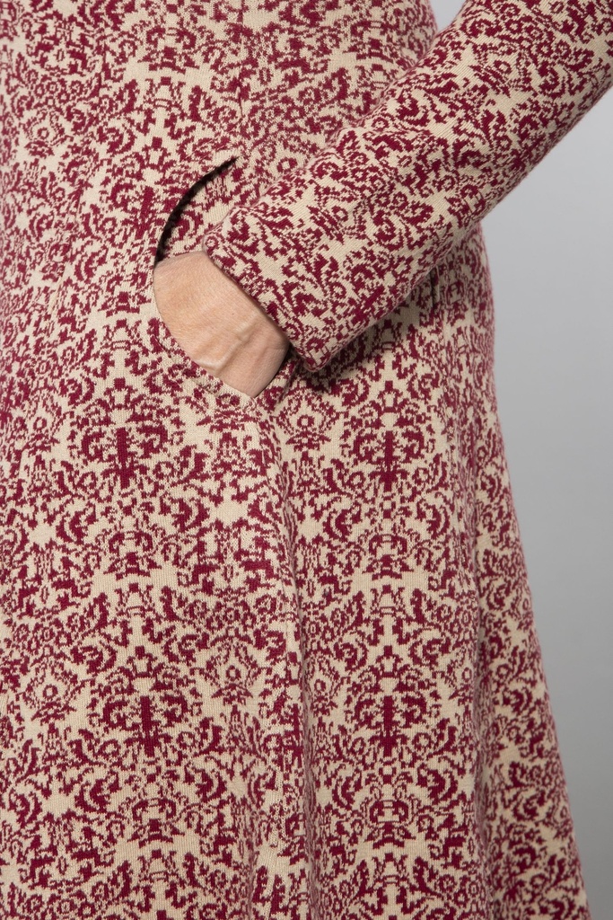 Ganzkörperansicht von vorn: knielanges Strickkleid mit rot-weißem Ornamentmuster, V-Ausschnitt, langärmelig, der Rock fällt leicht ausgestellt.