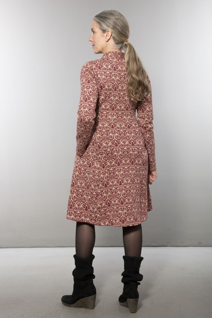 Ganzkörperansicht von vorn: knielanges Strickkleid mit rot-weißem Ornamentmuster, V-Ausschnitt, langärmelig, der Rock fällt leicht ausgestellt.