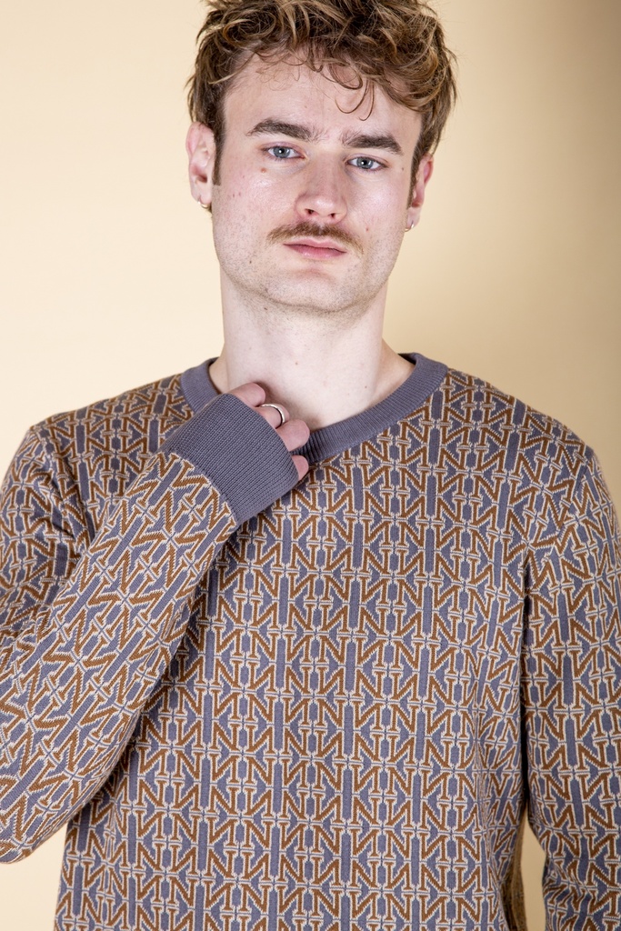 Nahaufnahme von Ausschnitt und Schulter: der braun-graue Pullover aus Strick-Jacquard zeigt eine graublaue Rippblende und feine Musterstreben.