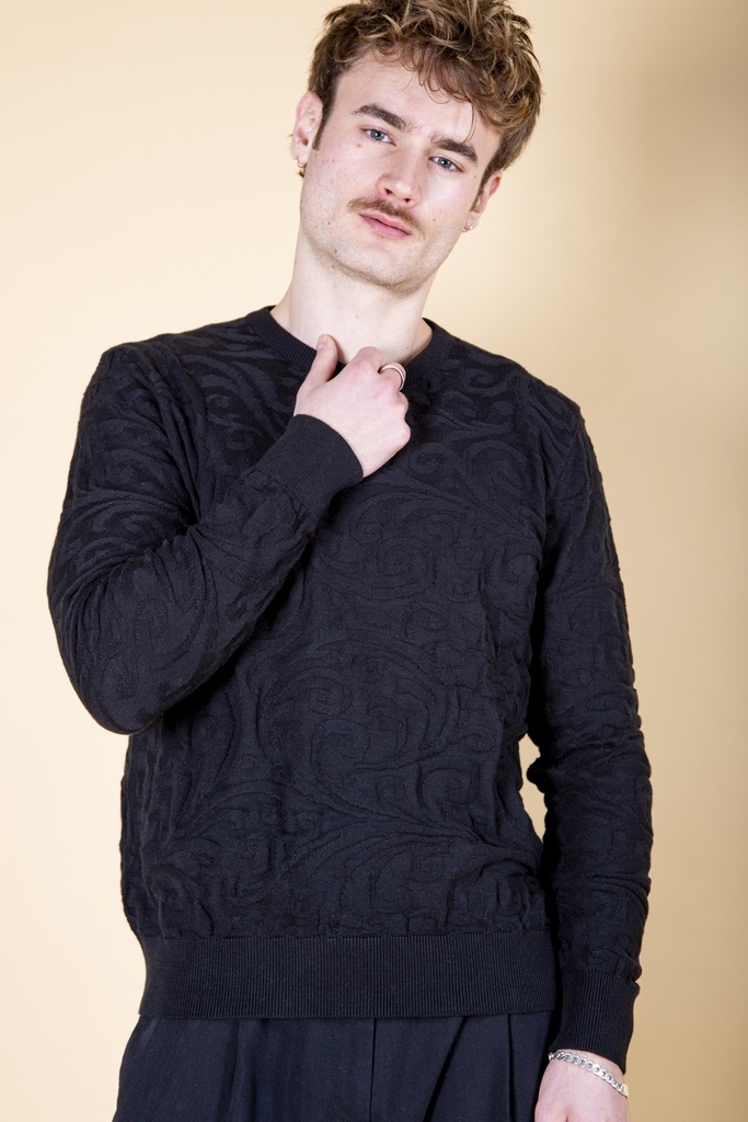 Vorderansicht bis zur Hüfte: schwarzer Pullover aus Strick-Jacquard mit reliefartigem Rankenmuster, Rundhalsausschnitt und breitem Rippbund.