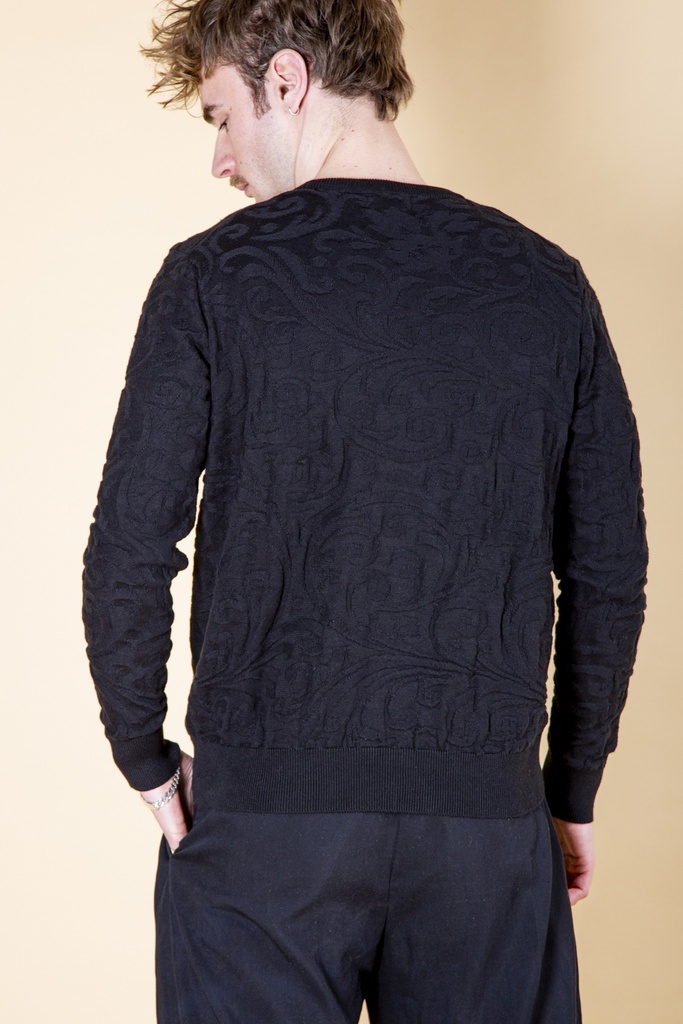 Rückansicht bis zur Hüfte: das reliefartige Rankenmuster bedeckt den schwarzen Strick-Jacquard-Pullover bis zum breiten gerippten Saum.