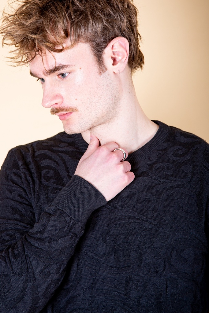 Nahaufnahme von Ausschnitt und Schulter: der schwarze Strick-Jacquard-Pullover hat einen schmalen Rundhalsausschnitt und reliefartige Ornamente.