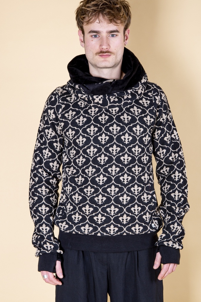 Vorderansicht bis zur Hüfte: schwarzer Pullover aus Strick-Jacquard mit weißen Lilien, Kapuzenschal und schwarzen Stulpen über den Händen.