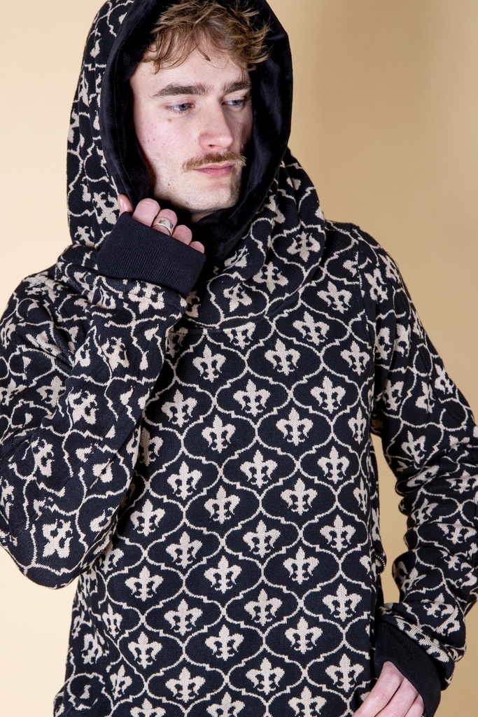 Nahaufnahme mit aufgesetzter Kapuze: der schwarz-weiß gemusterte Pullover aus Strick-Jacquard zeigt den weichen Kapuzenrand und schwarze Stulpen.