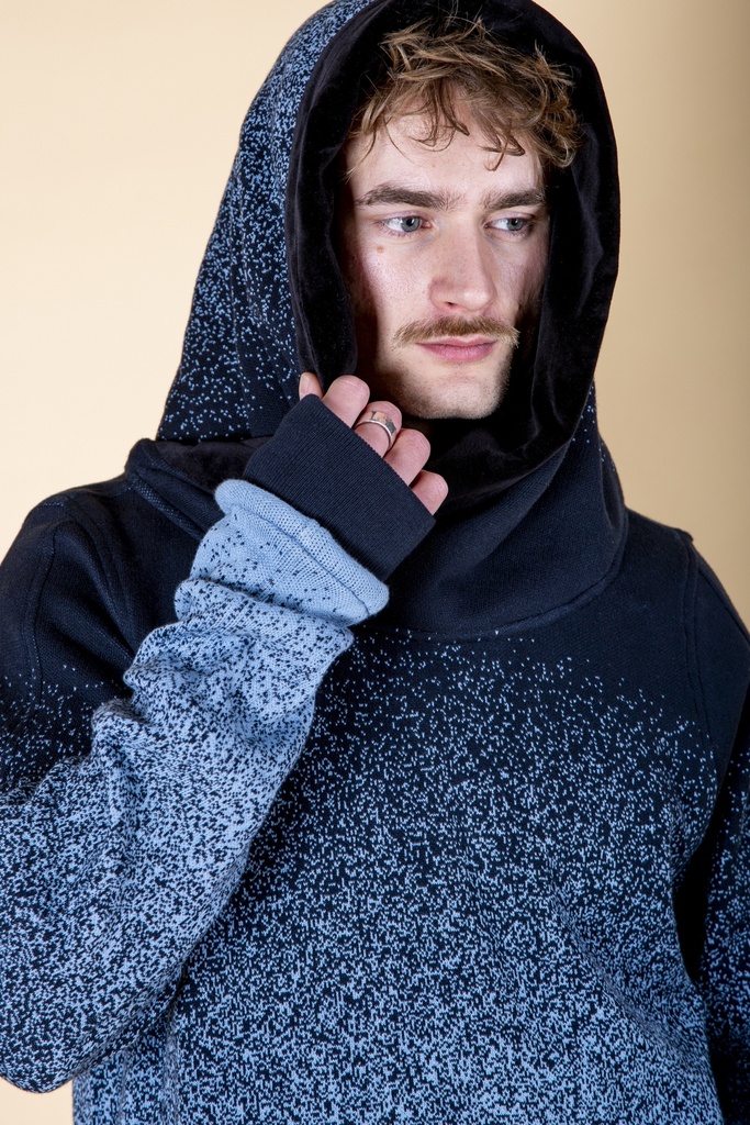 Nahaufnahme mit aufgesetzter Kapuze: der blau verlaufende Pullover aus Strick-Jacquard zeigt eine schwarze Ärmelstulpe mit Daumenloch.