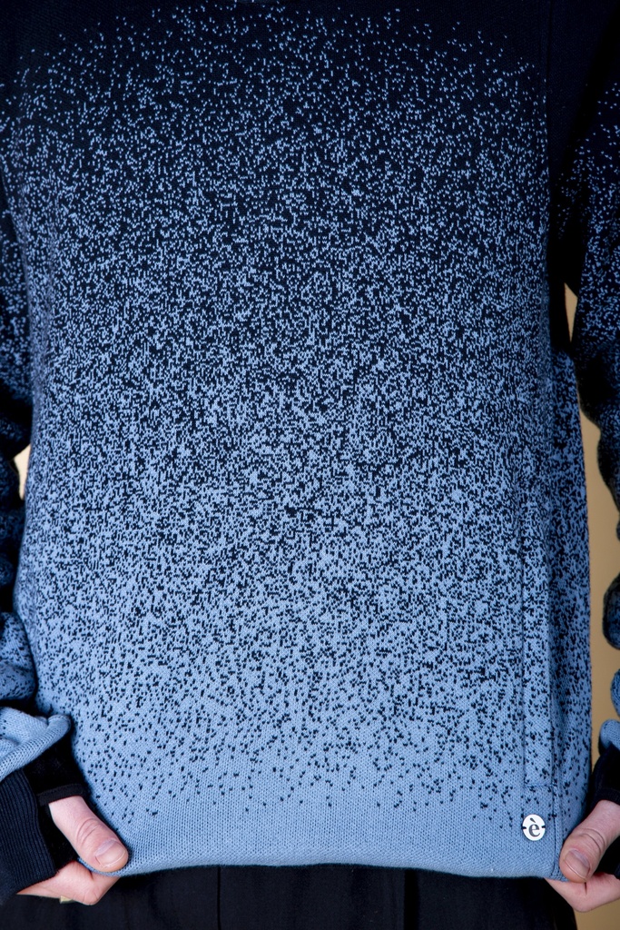 Makroaufnahme des Vorderteils: am blau verlaufenden Pullover aus Strick-Jacquard verdichten sich dunkle Sprenkel zur Schulter, der Saum ist hellblau.