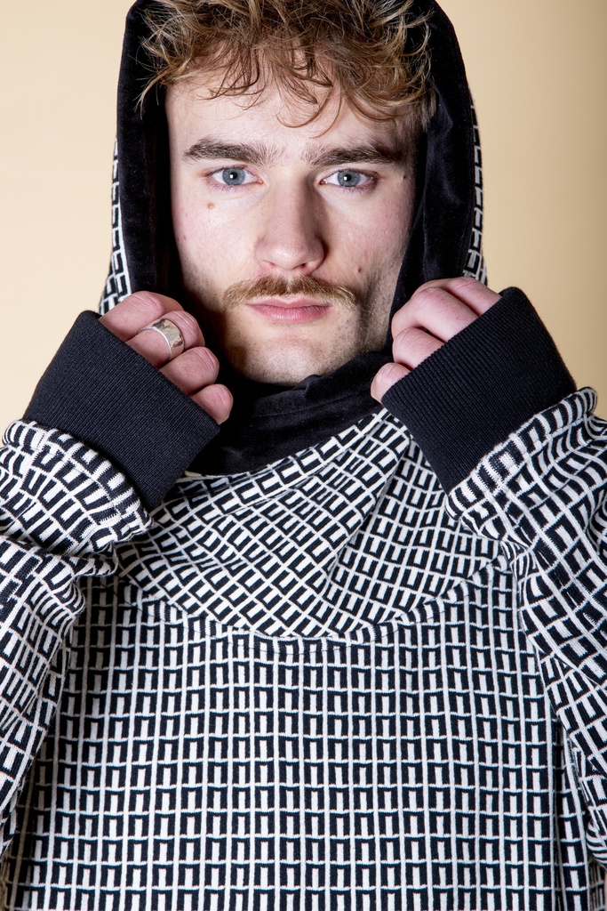 Nahaufnahme mit aufgesetzter Kapuze: der schwarz-weiß gemusterte Pullover aus Strick-Jacquard zeigt schwarzen Kapuzenschal und Ärmelstulpen.
