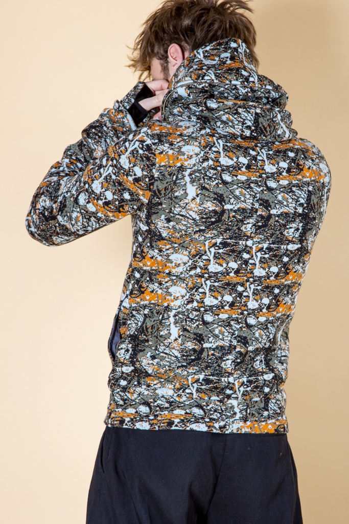 Rückansicht bis zur Hüfte: das orange-grau-schwarze Fleckenmuster bedeckt den Rücken der Strick-Jacquard-Jacke bis unter die hohe Kapuze.