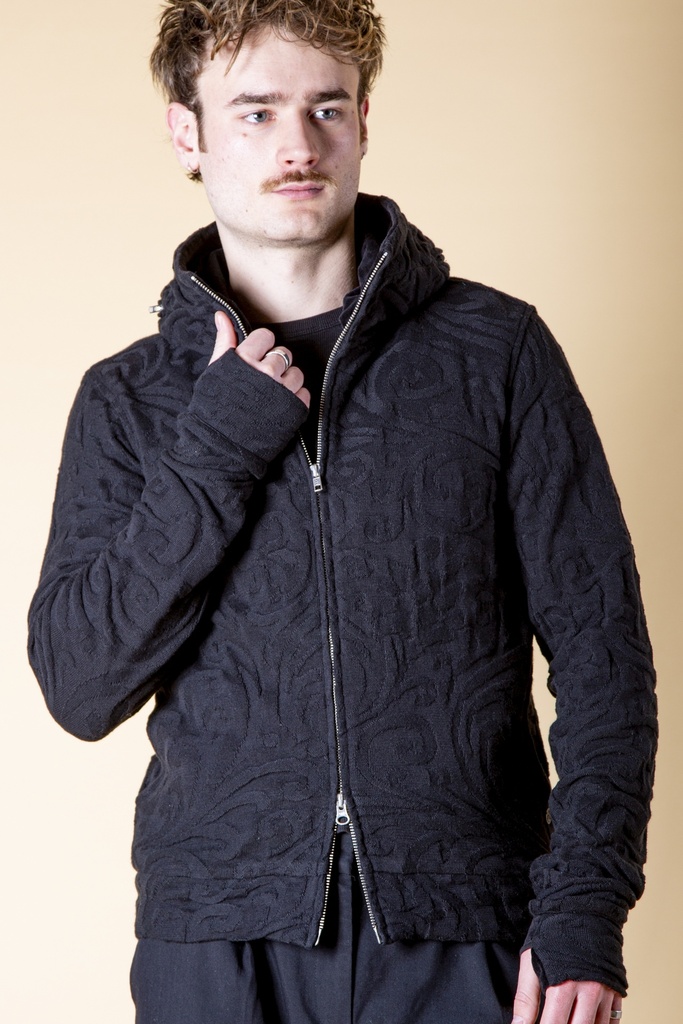 Vorderansicht bis zur Hüfte: schwarze Strick-Jacquard-Jacke mit Reißverschluss, reliefartigem Muster, Eingrifftasche und Ärmelstulpen.