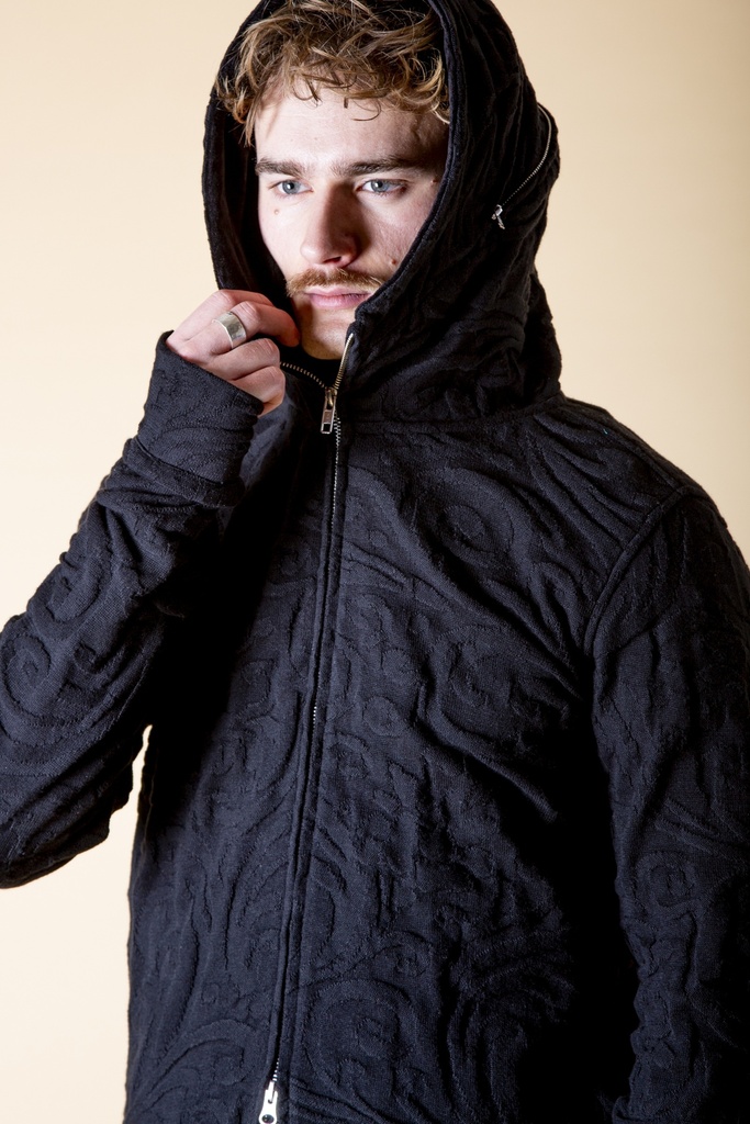 Nahaufnahme mit aufgesetzter Kapuze: die schwarze Strick-Jacquard-Jacke zeigt die Kapuze am Reißverschluss über dem hohen Schalkragen.