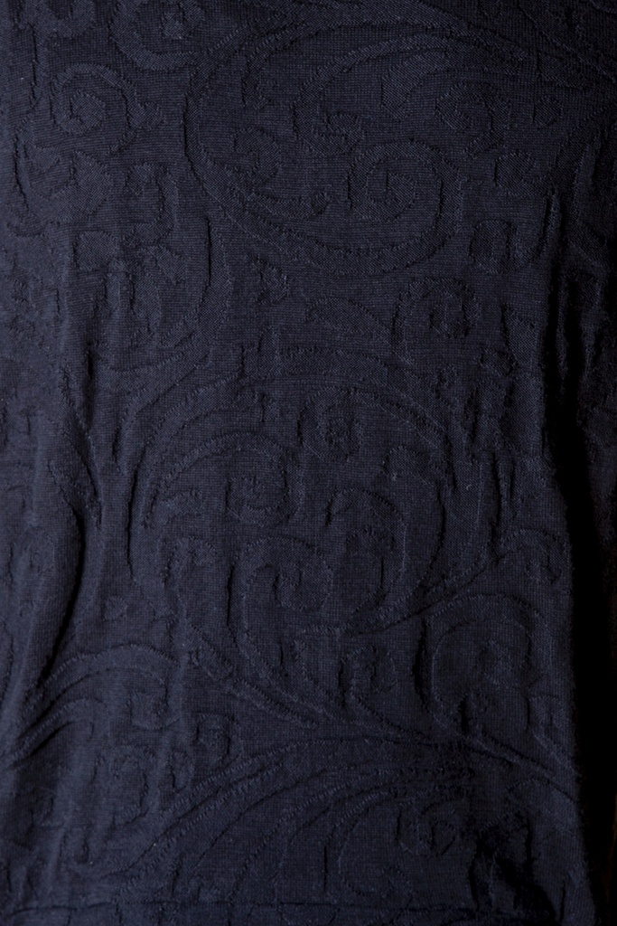 Makroaufnahme der Jackenoberfläche: Ranken und Bögen heben sich als reliefartiges Muster im schwarzen Strick-Jacquard ohne Farbwechsel ab.