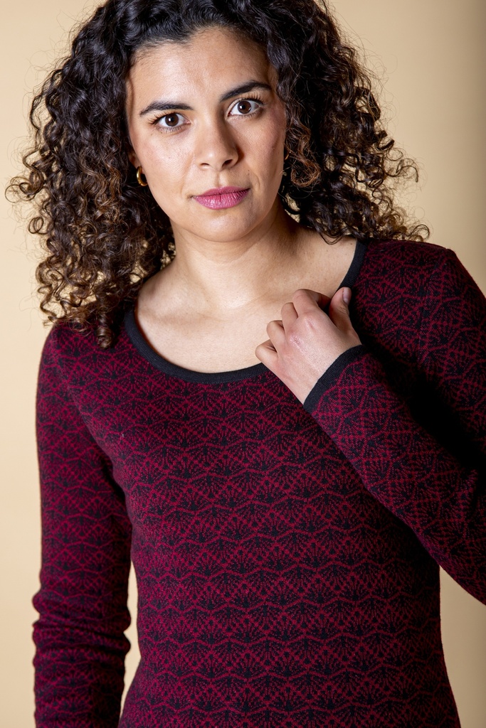 Nahaufnahme von Ausschnitt und Schulter: der dunkelrote Strick-Jacquard-Pullover hat eine schwarze Rundhalskante über kleinteiligem Rankenmuster.