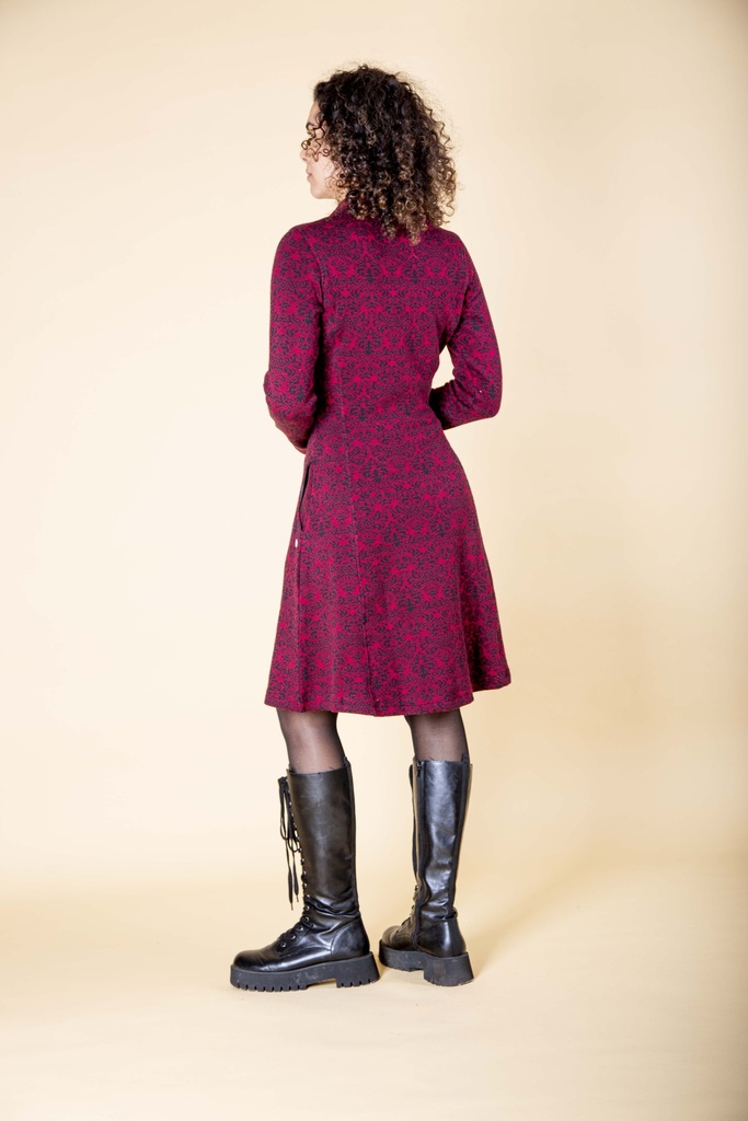 Rückansicht in ganzer Länge: das dunkelrote Strick-Jacquard-Kleid mit schwarzem Barockmuster fällt ab der Taille in eine schwingende A-Linie.