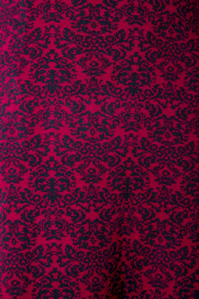 Makroaufnahme des Kleid-Stricks: schwarze Barockornamente stehen spiegelsymmetrisch in dichten Reihen auf dunkelrotem Jacquardgrund.