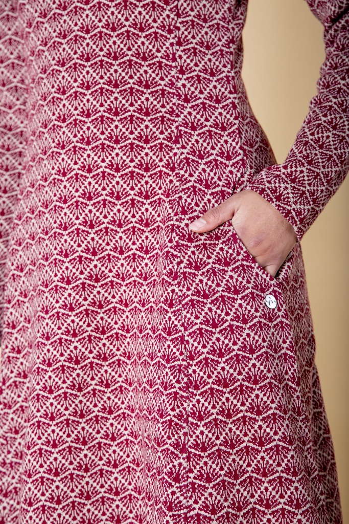 Nahaufnahme der Hüfte: eine Hand steckt in der seitlichen Eingrifftasche des weiß-dunkelrot gemusterten Strick-Jacquard-Kleids neben hellem Knopf.