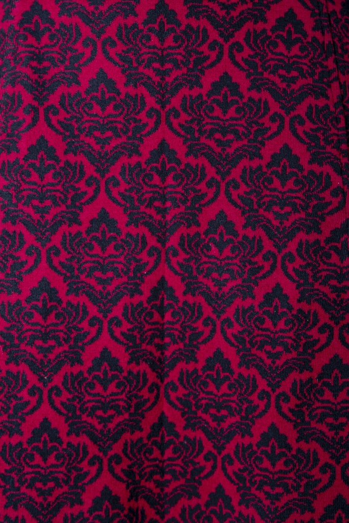 Makroaufnahme des Stoffs: weinrotes Kleid aus Strick-Jacquard mit dichtem schwarzem Ornamentmuster in der fein gestrickten Oberfläche.