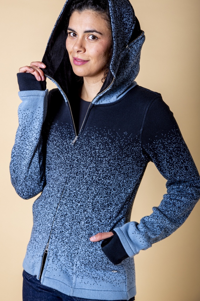 Vorderansicht mit aufgesetzter Kapuze: die blau verlaufende Strick-Jacquard-Jacke zeigt den hohen Reißverschlusskragen und schwarze Ärmelstulpen.