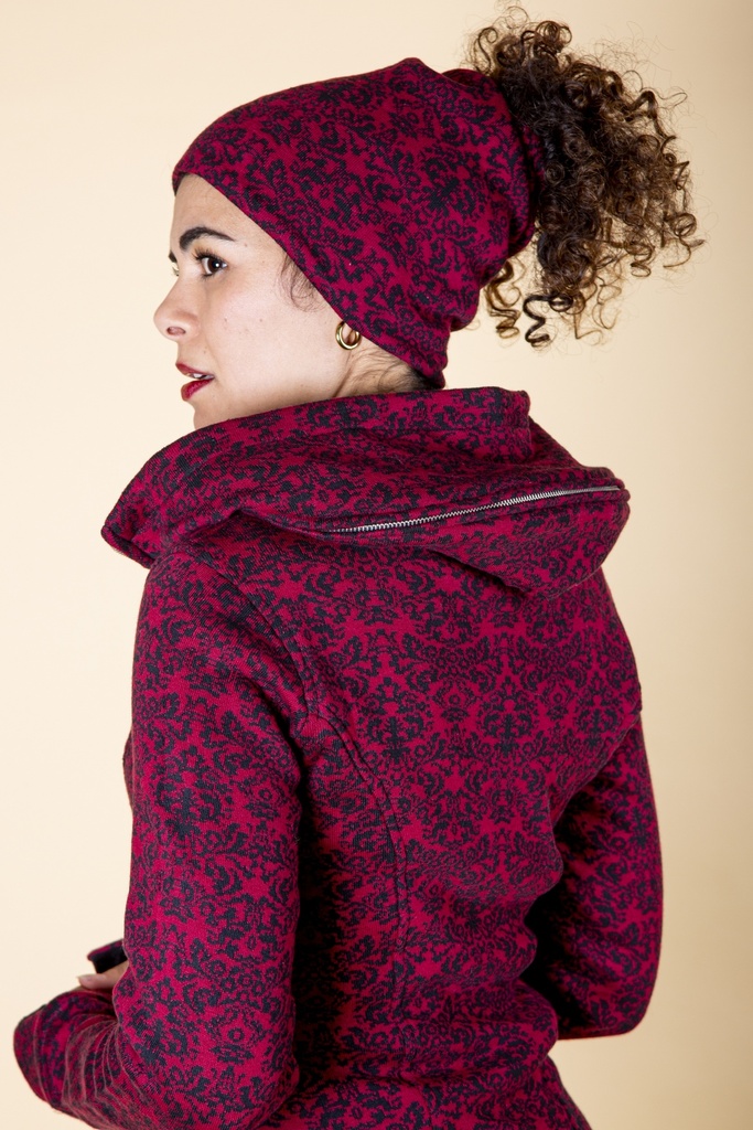 Ansicht von schräg hinten: die Mütze und der breite Kragen der Jacke zeigen dasselbe rot-dunkle Ornamentmuster.