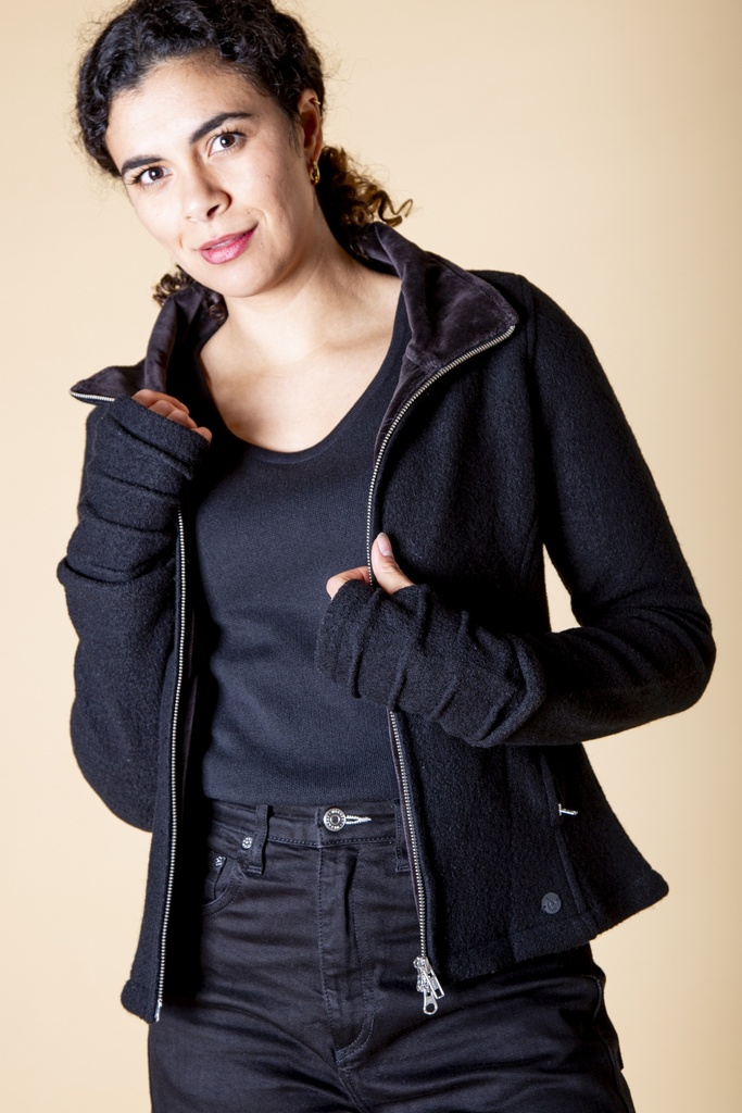 Oberkörper halbnah: kurze schwarze Wolljacke mit schrägem Reißverschluss und Stehkragen, offen über einem schwarzen Shirt getragen.