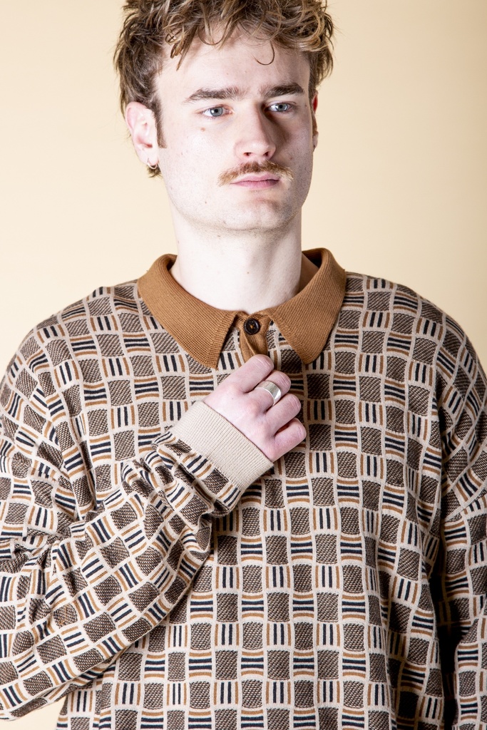 Detailansicht von vorn: Das beigebraune Poloshirt zeigt den braunen Strickkragen, die kurze Knopfleiste und das grafische Jacquardmuster.