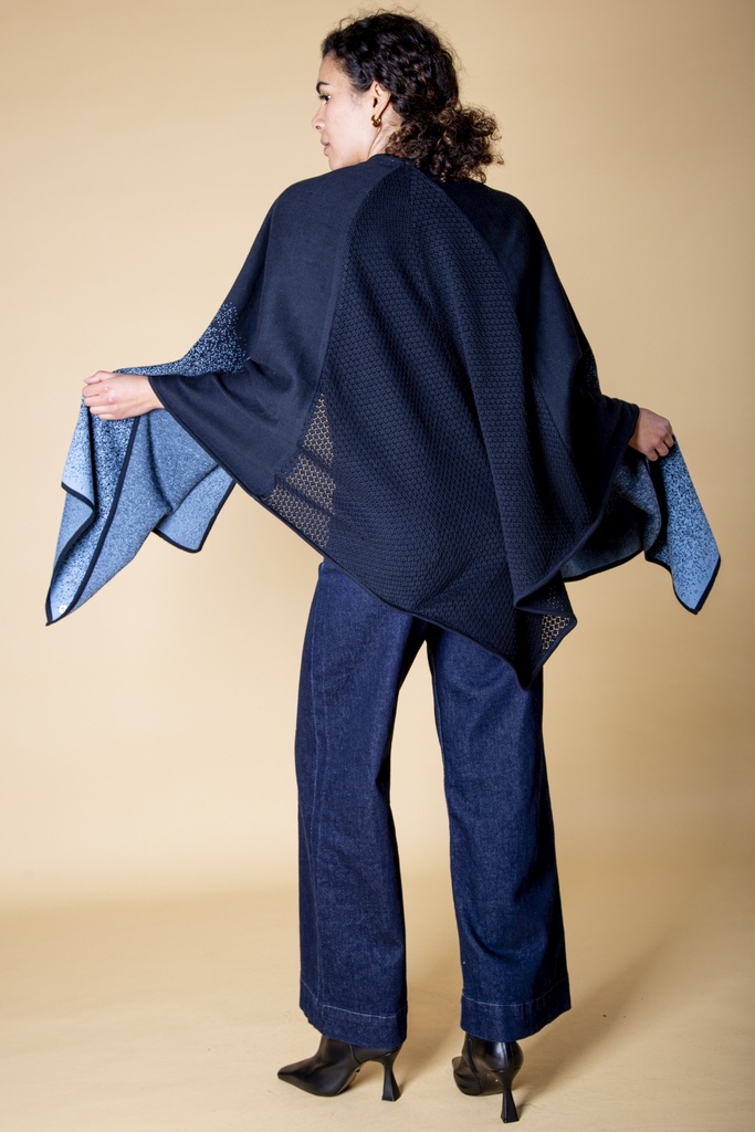 Rückansicht mit ausgebreiteten Armen: der dunkelblaue Poncho öffnet sich zu hellblau gesprenkelten Spitzen über dem gehäkelten Rückenteil.