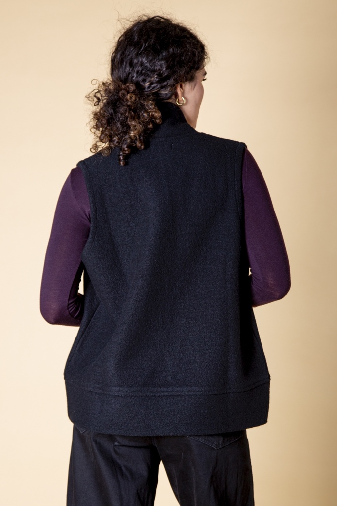 Rückansicht bis zur Hüfte: die schwarze Merinowollweste fällt gerade und endet mit einem breiten, glatt gestrickten Saumbund.