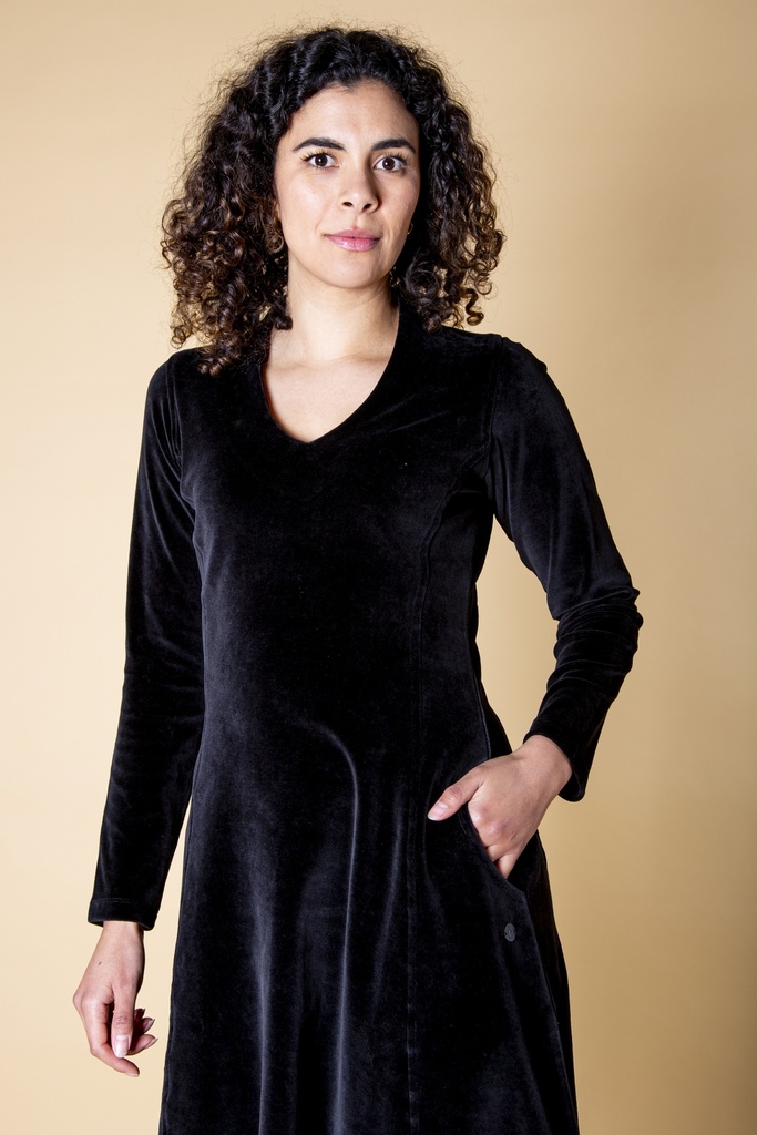 Halbnahe Ansicht von vorn: Das schwarze Kleid aus Samt zeigt den V-Ausschnitt, die langen Ärmel und die seitliche Eingrifftasche mit Knopfleiste.