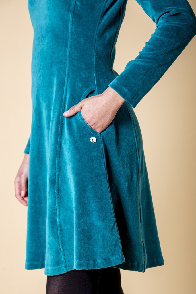Detailansicht: Das petrolblaue Kleid aus Samt zeigt eine seitliche Eingrifftasche mit einer kleinen silberfarbenen Knopfleiste am ausgestellten Rockteil.