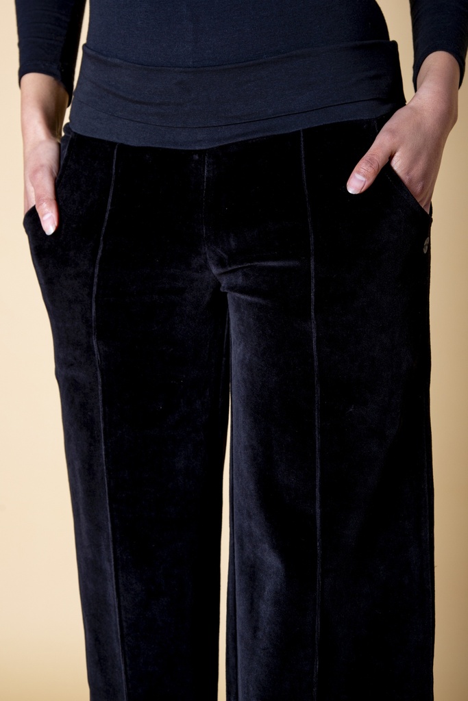 Nahaufnahme der Hüfte: beide Hände stecken in den Eingrifftaschen der schwarzen Samthose, mittige Biesen beginnen unter dem elastischen Bündchen.