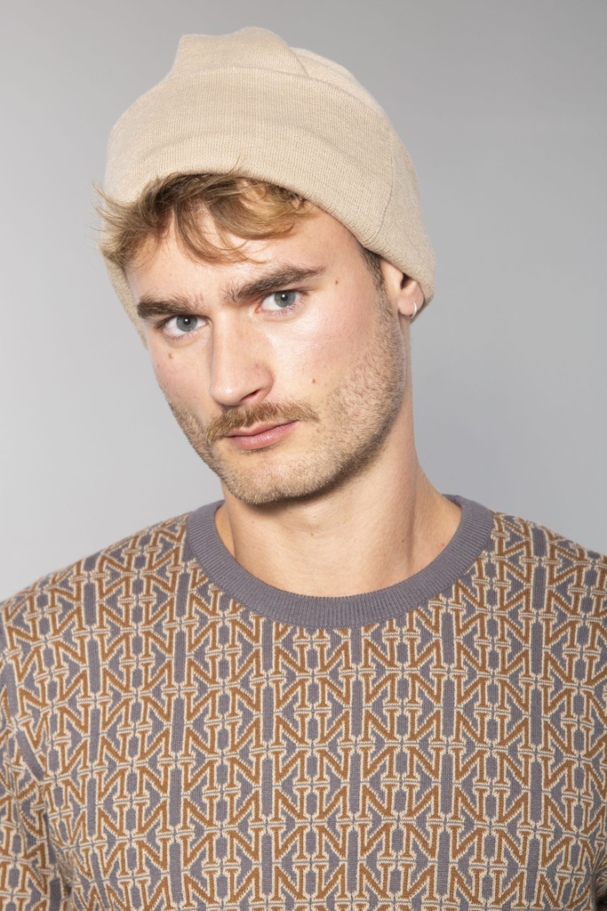Beigefarbene Strickmütze mit umgeschlagenem Rand, an einem Mann getragen, der einen gemusterten Pullover trägt.