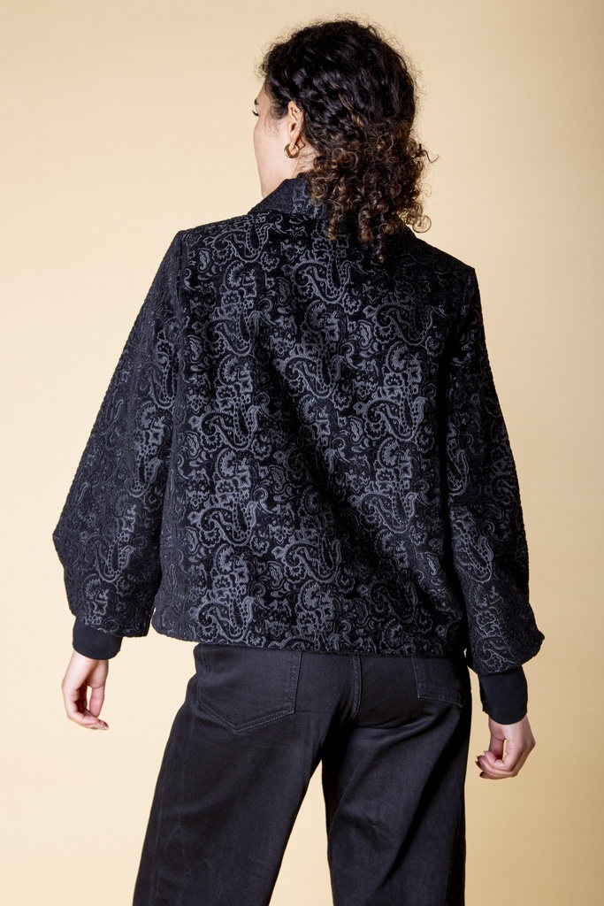 Rückansicht bis zur Hüfte: das silbergraue Paisley-Muster bedeckt den lockeren schwarzen Rücken der Brokatjacke bis zum dunklen Saum.