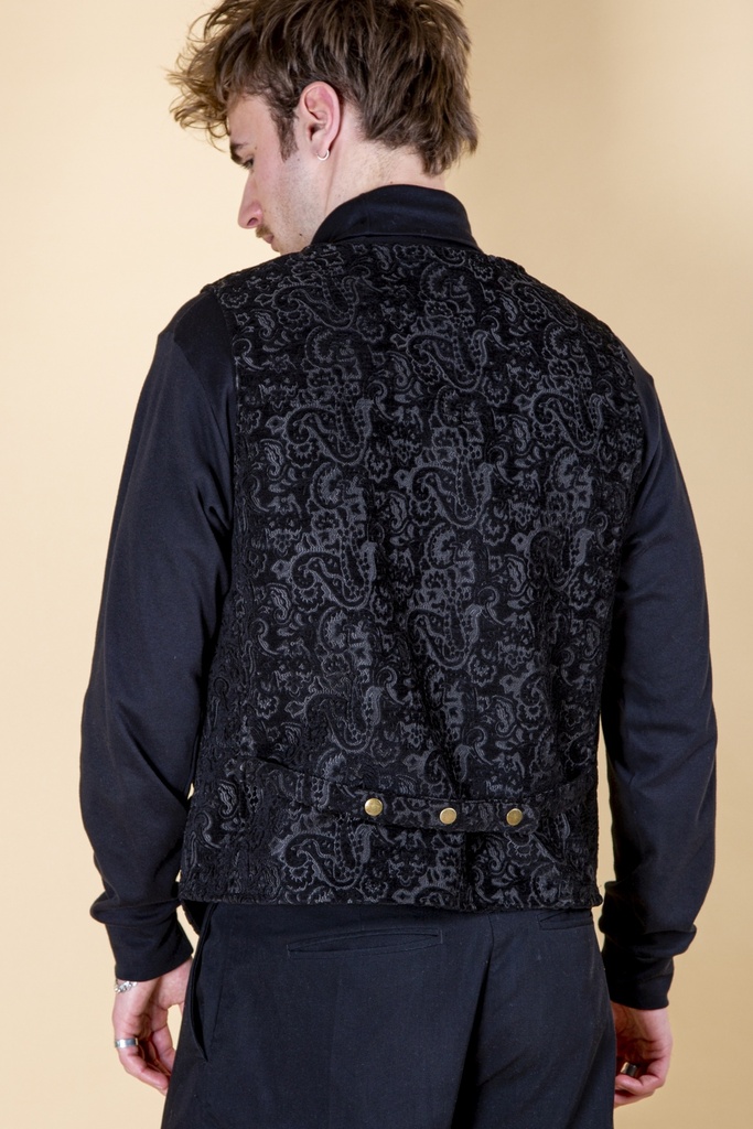 Rückansicht bis zur Hüfte: das silbergraue Paisley-Muster bedeckt den schwarzen Rücken der Weste, goldfarbene Druckknöpfe sitzen am Saumbund.