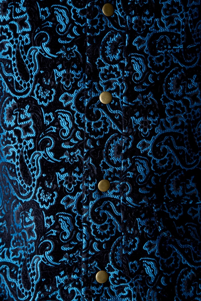 Makroaufnahme des Brokats: türkisfarbene Paisley-Ornamente heben sich auf schwarzem Grund ab, mittig verläuft die goldfarbene Druckknopfleiste.