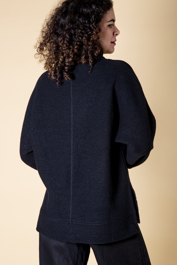 Rückansicht bis zur Hüfte: der schwarze Pullover fällt locker, eine senkrechte Naht gliedert den Rücken zwischen den überschnittenen Schultern.