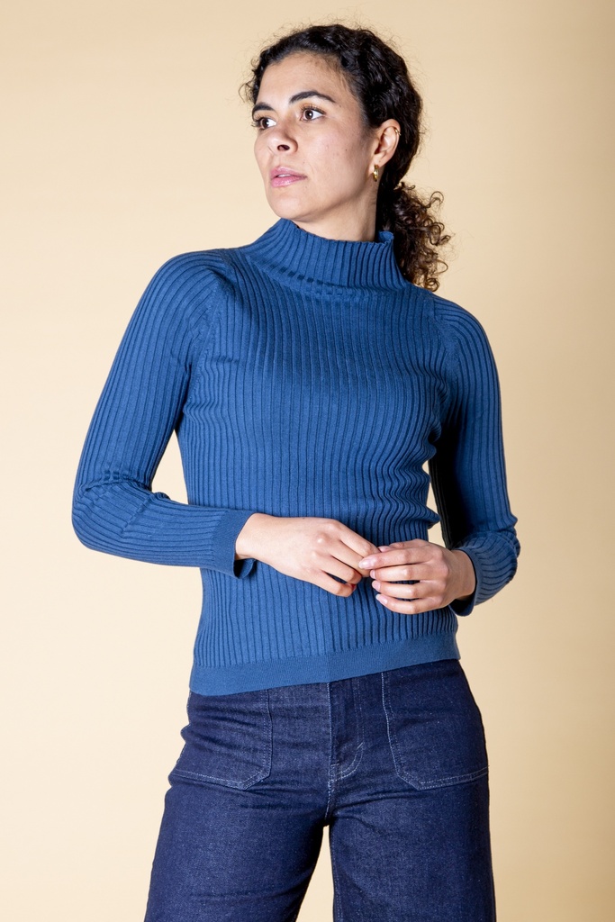 Oberkörperansicht schräg von vorn: Der kräftig blaue Pullover zeigt Rollkragen, schmale Längsrippen und eine körpernahe Silhouette.