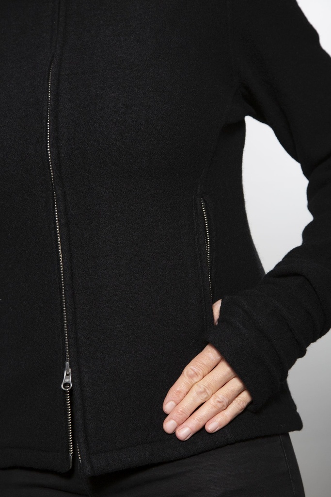 Oberkörper halbnah: kurze schwarze Wolljacke mit schrägem Reißverschluss und Stehkragen, offen über einem schwarzen Shirt getragen.