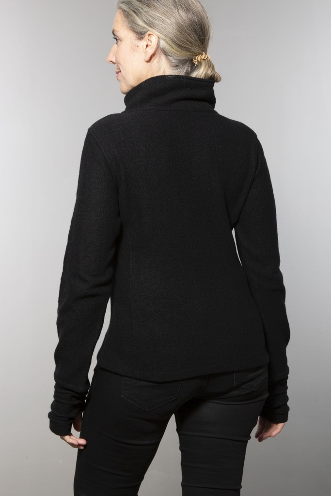 Oberkörper halbnah: kurze schwarze Wolljacke mit schrägem Reißverschluss und Stehkragen, offen über einem schwarzen Shirt getragen.