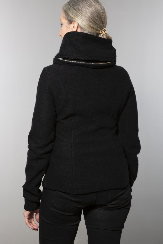 Ganzkörperansicht von vorn: die taillierte schwarze Wolljacke endet an der Hüfte, dazu eine schwarze weite Hose.