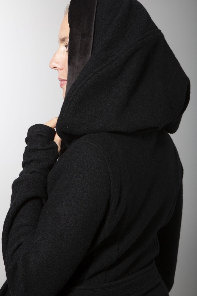Ganzkörperansicht von vorn: schwarzer Wollmantel bis übers Knie mit Bindegürtel und großer Kapuze, deren Innenseite grau abgesetzt ist.