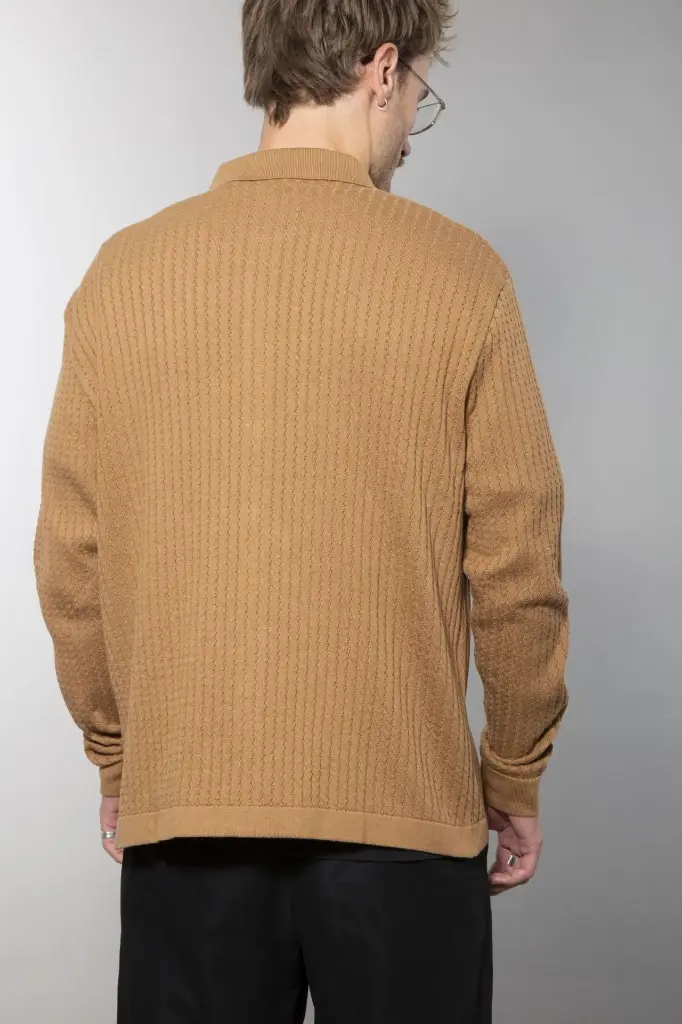 Ganzkörperansicht von vorn: schwarze Strickjacke mit Hemdkragen und Knopfleiste, senkrechte Rippenstruktur, dazu eine dunkle weite Hose.