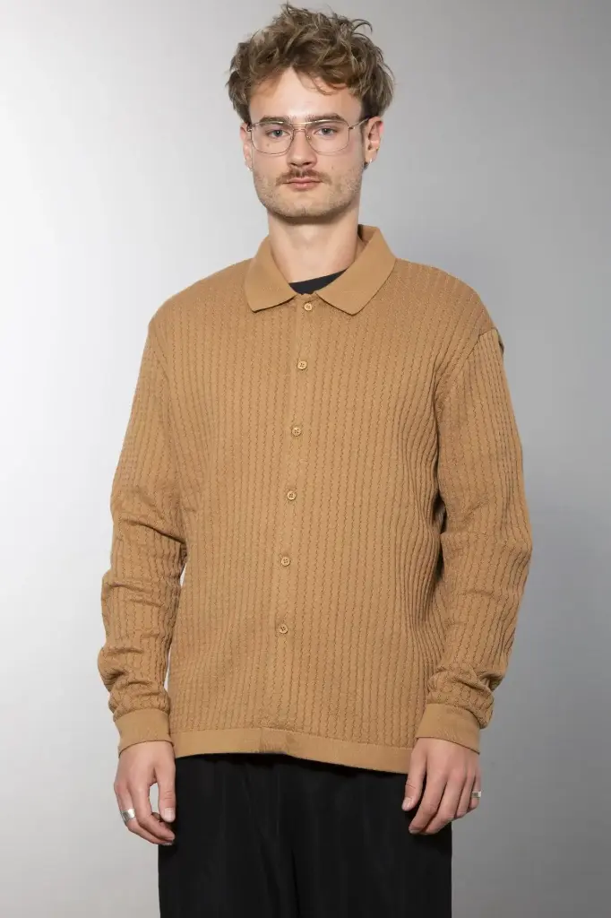Ganzkörperansicht von vorn: schwarze Strickjacke mit Hemdkragen und Knopfleiste, senkrechte Rippenstruktur, dazu eine dunkle weite Hose.